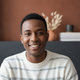 A smiling person in their late 20s or early 30s, with a blurred background in terracotta and charcoal tones.